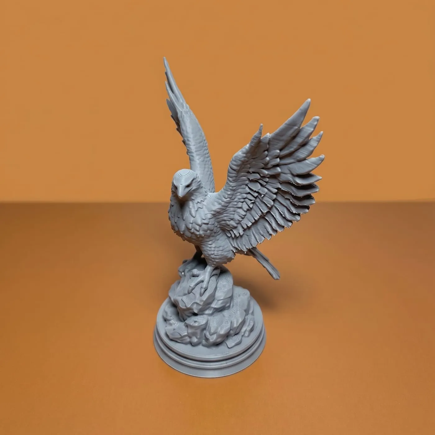 Figura de un águila con las alas abiertas sobre una base de roca, impresa en PLA gris